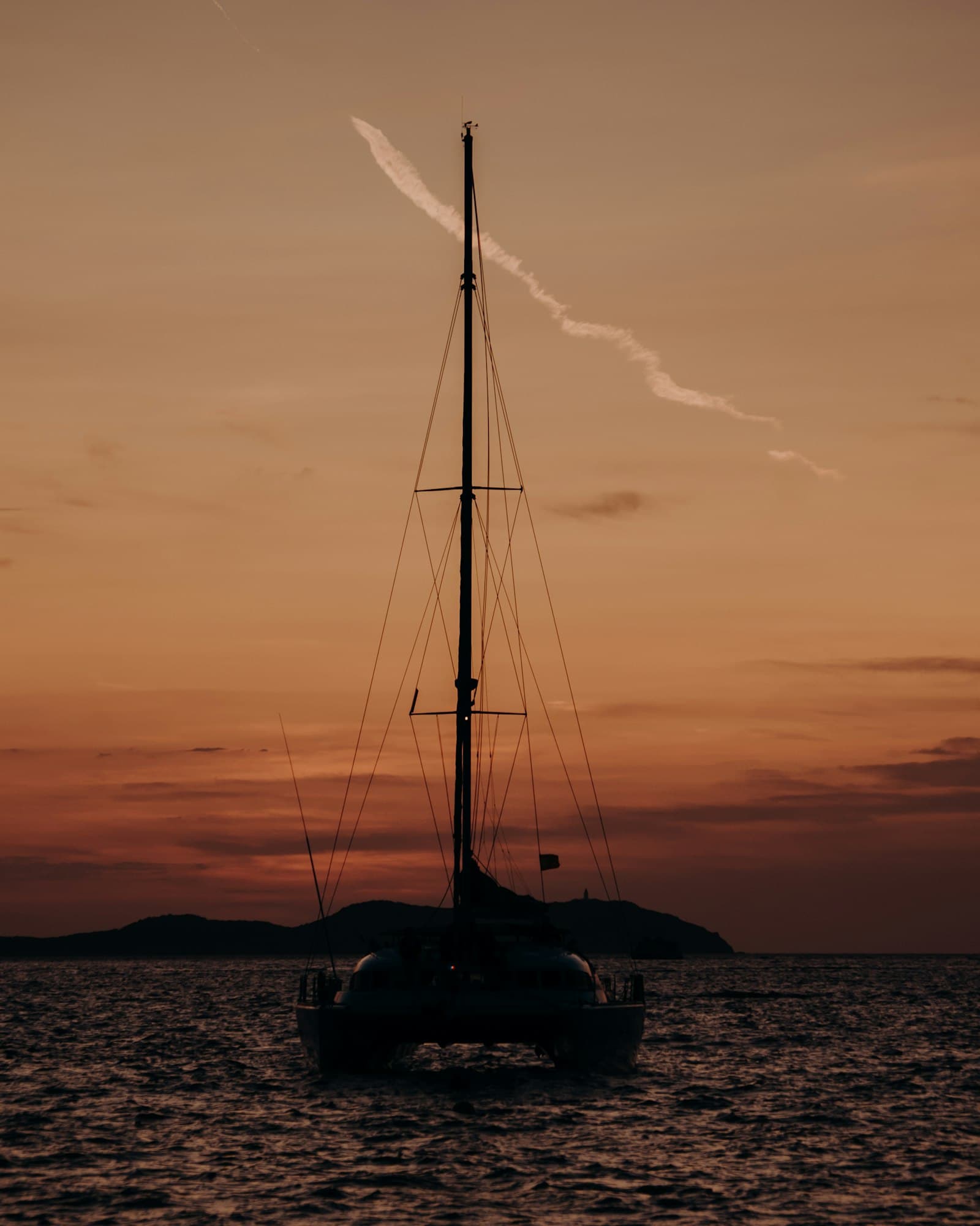 Silhouetted sailing catamaran anchored on calm water beneath a soft amber sunset sky