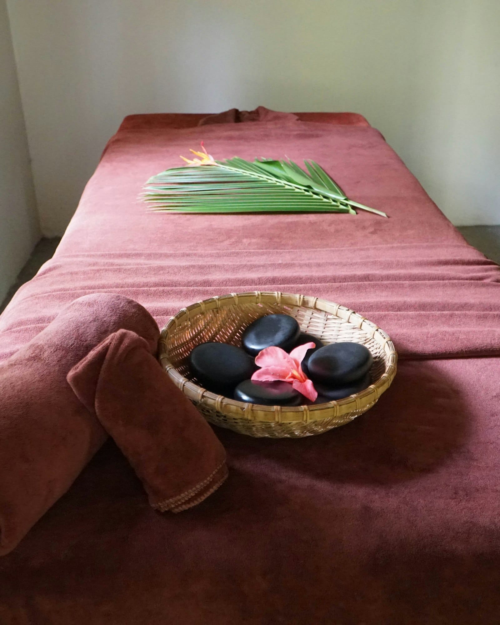 Massage table with terracotta towels, basket of hot stones, hibiscus flower and palm frond